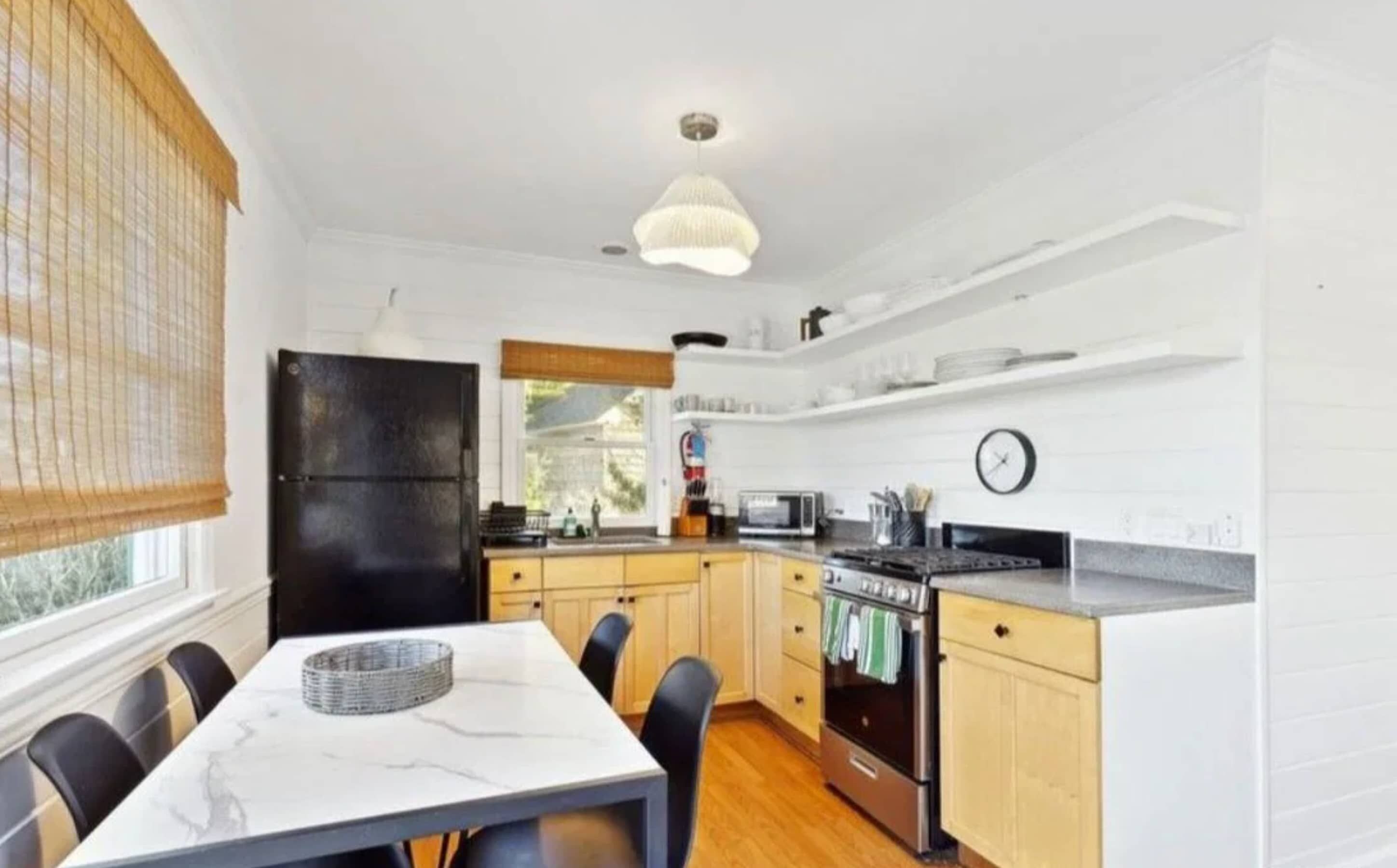 A compact kitchen with a dining table, chairs, a refrigerator, a stove, and a hanging light fixture.
