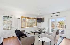 A modern living room with a sofa, armchairs, a coffee table, and a flat-screen TV mounted on the wall. - Cozy Cottage by the beach - Seabreeze #1 (Hampton Bays)