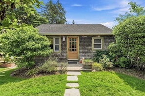 A single-story house with a front door, a small porch, and a stone pathway leading to the entrance. - Cozy Cottage by the beach - Seabreeze #1 (Hampton Bays)
