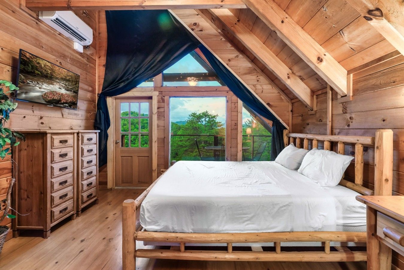 Un dormitorio de madera con una cama, un aparador y una ventana con vistas a la vegetación.