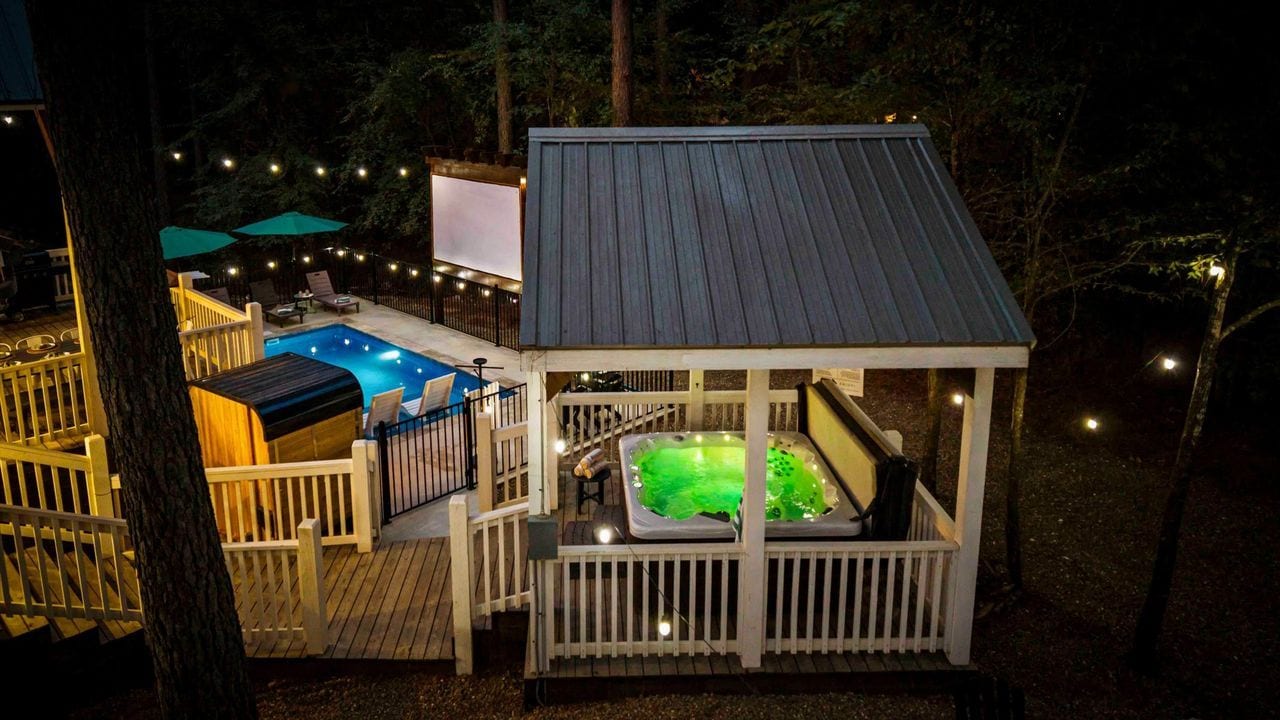 A deck with a hot tub and a pool, surrounded by trees and string lights.