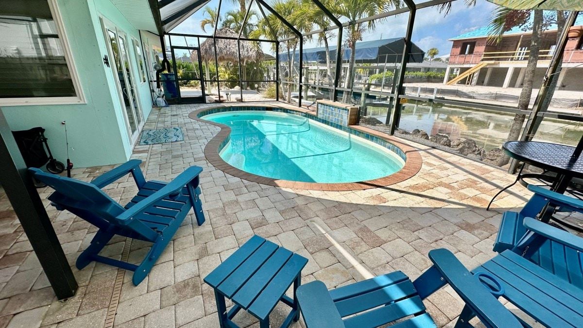 An outdoor pool area with blue chairs and a table, surrounded by a glass enclosure with a view of the landscape.