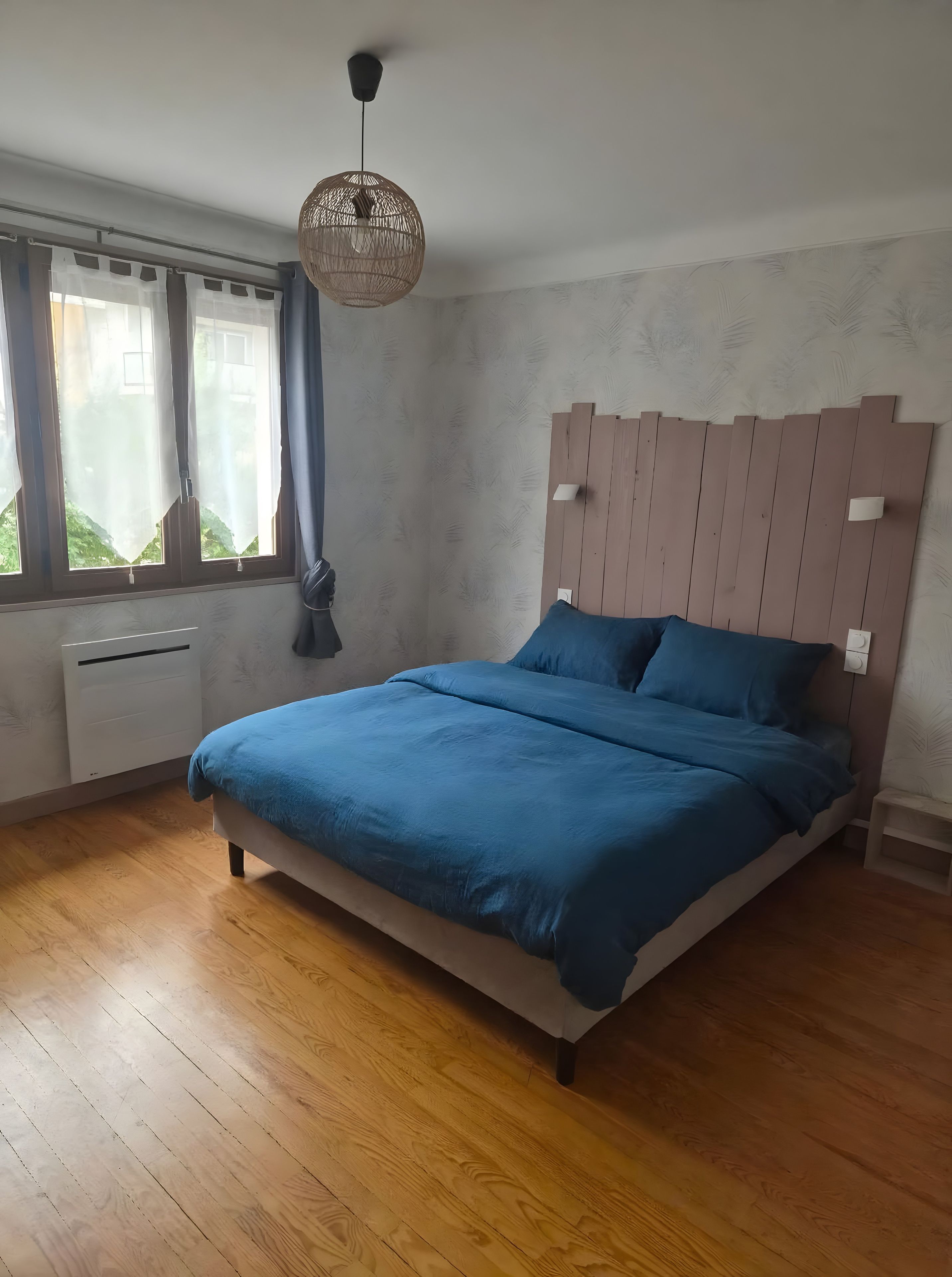 Een slaapkamer met een bed, een raam met gordijnen, een plafondlamp en een wandheater.