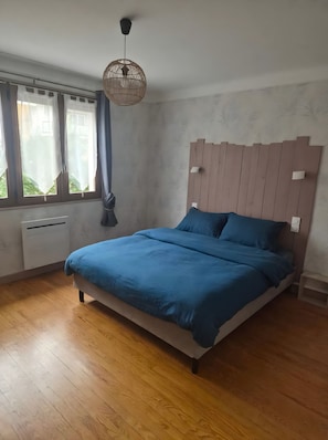 Une chambre à coucher avec un lit, une fenêtre avec des rideaux, un luminaire au plafond et un radiateur fixé au mur.