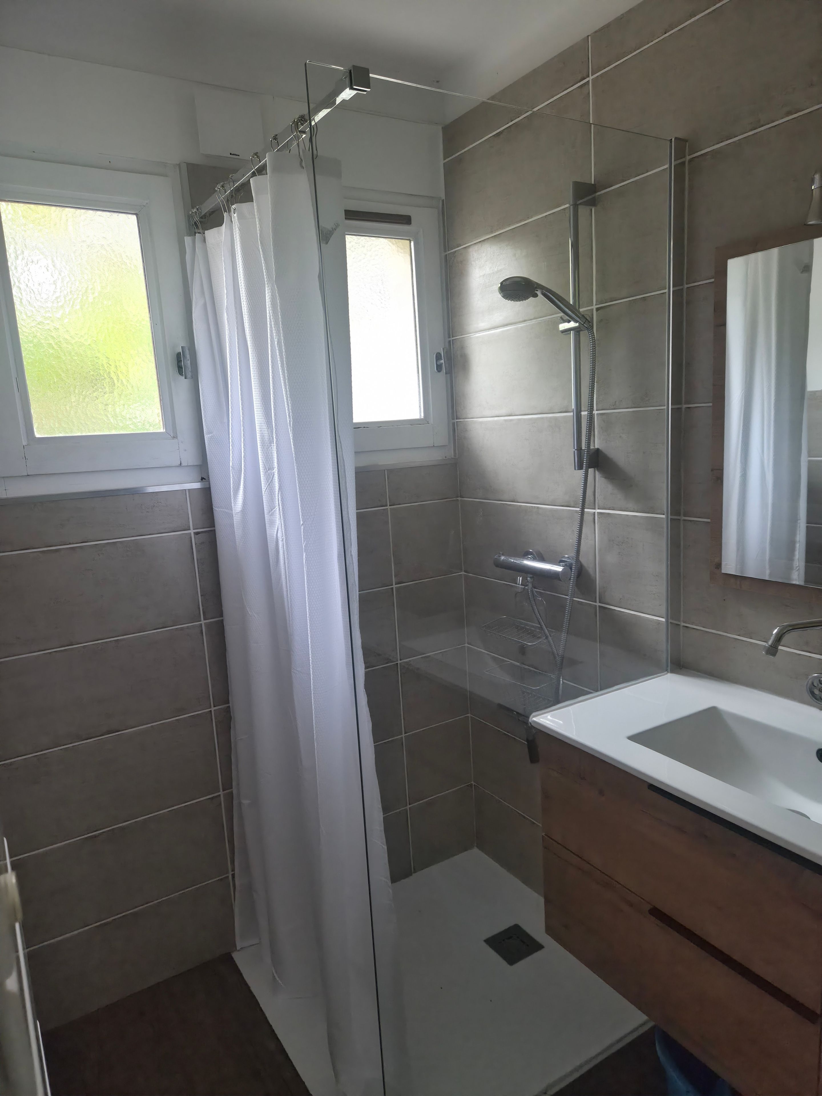 Een moderne badkamer met een douche, wastafel en raam.