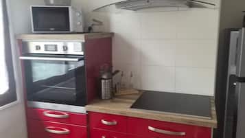 A kitchen with red cabinets, a microwave, an oven, and a stainless steel range hood.