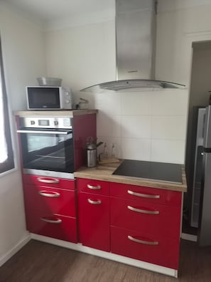 Une cuisine avec des meubles de couleur rouge, un four à micro-ondes, un four traditionnel et une hotte de cuisson en acier inoxydable.