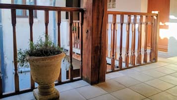 Un balcon en bois orné d’un pot de fleurs, un sol carrelé et une vue sur un immeuble avec une fenêtre et une porte.