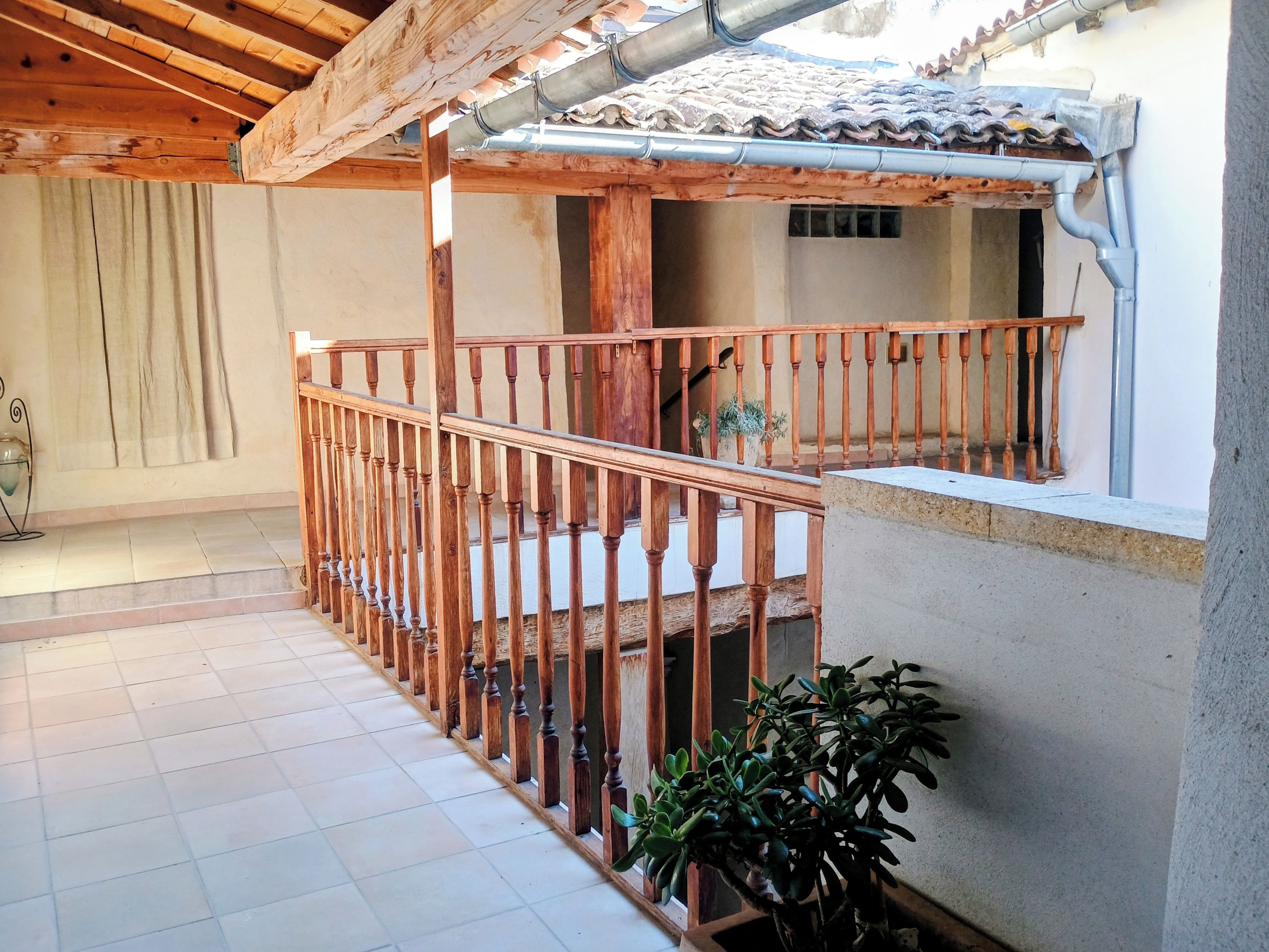 Un balcon en bois avec une balustrade, un sol carrelé et un pot de fleurs.