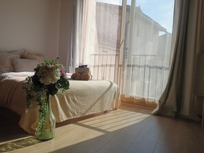 A bedroom with a bed, a vase with flowers, and a view of the outside. - New Listing (L'Isle-sur-la-Sorgue)