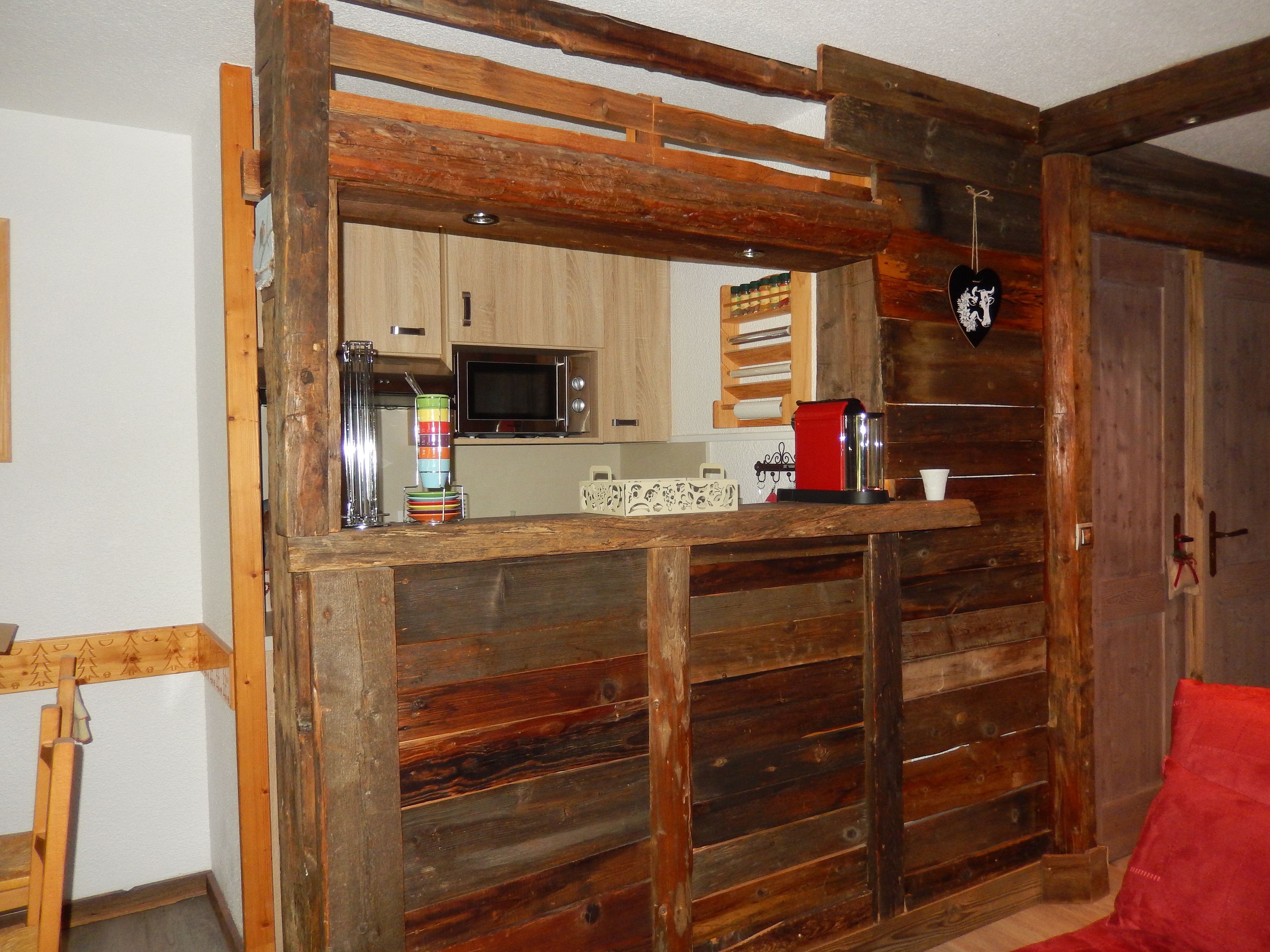 A rustic wooden partition with a kitchen area visible through a window, including a microwave and a red coffee maker.