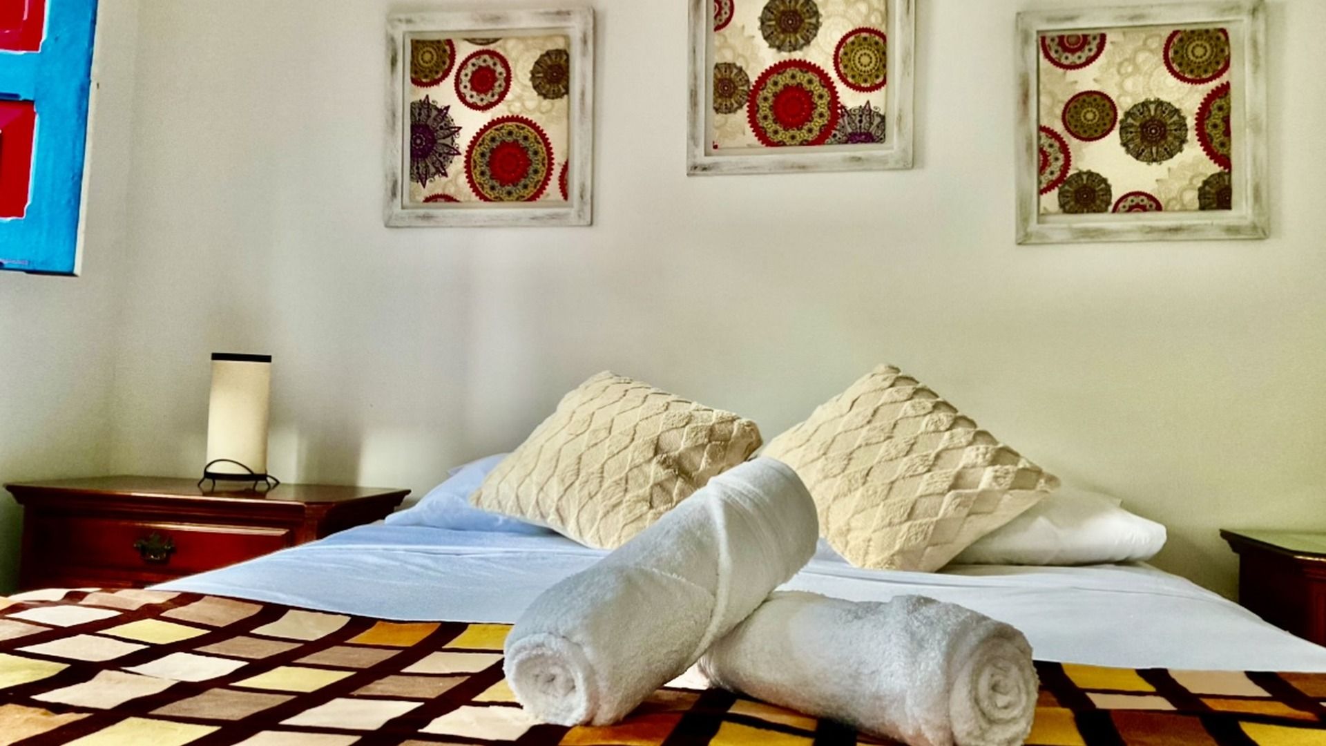 Camera d'albergo con un letto, due cuscini, un comodino, una lampada e tre decorazioni appese al muro.