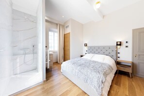 Ein modernes Schlafzimmer mit einer Marmordusche, einem großen Bett mit einem gepolsterten Kopfteil und Holzboden.