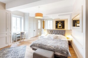 Ein Schlafzimmer mit einem großen Bett, einem Schreibtisch und einem Sessel. An der Wand befindet sich ein Spiegel und von der Decke hängt ein Kronleuchter.