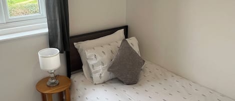 A single bed with a white bedspread and a small bedside table with a lamp.