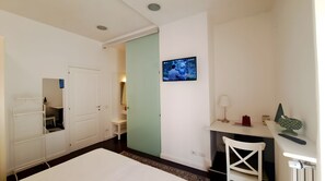 Una habitación de hotel con cama, escritorio, silla, televisor y armario.