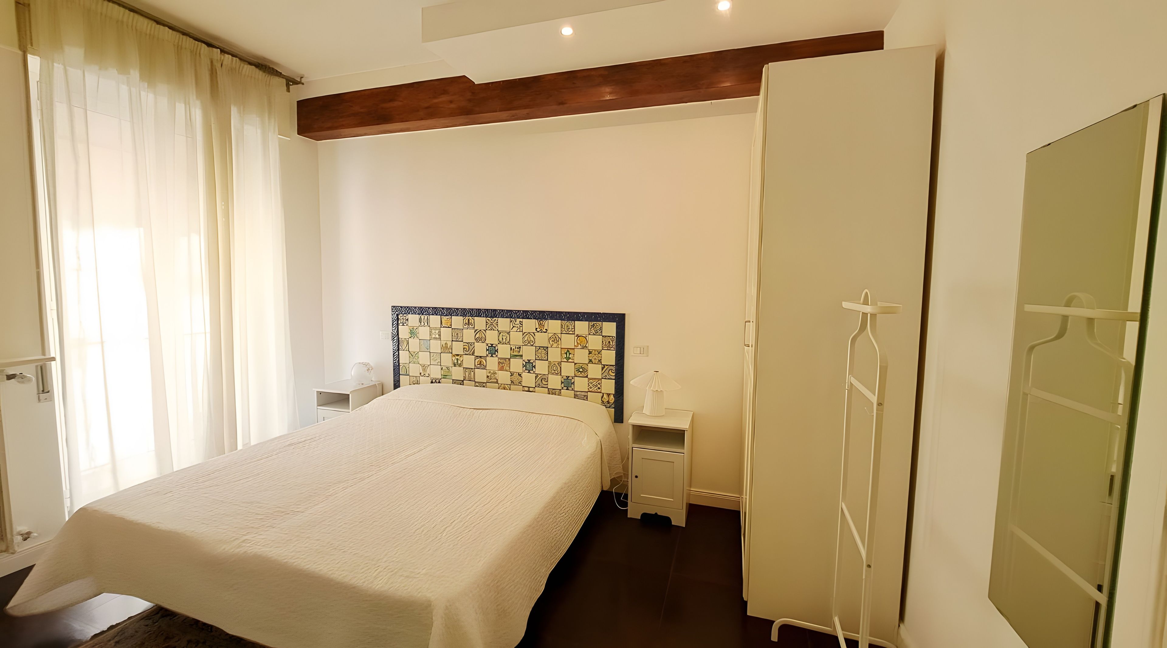 A hotel room with a bed, a nightstand, a wardrobe, and a window with curtains.