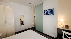 A hotel room with a bed, a desk with a lamp, a television, and a wardrobe. - Casa Alba - Mara Room (Caltagirone)