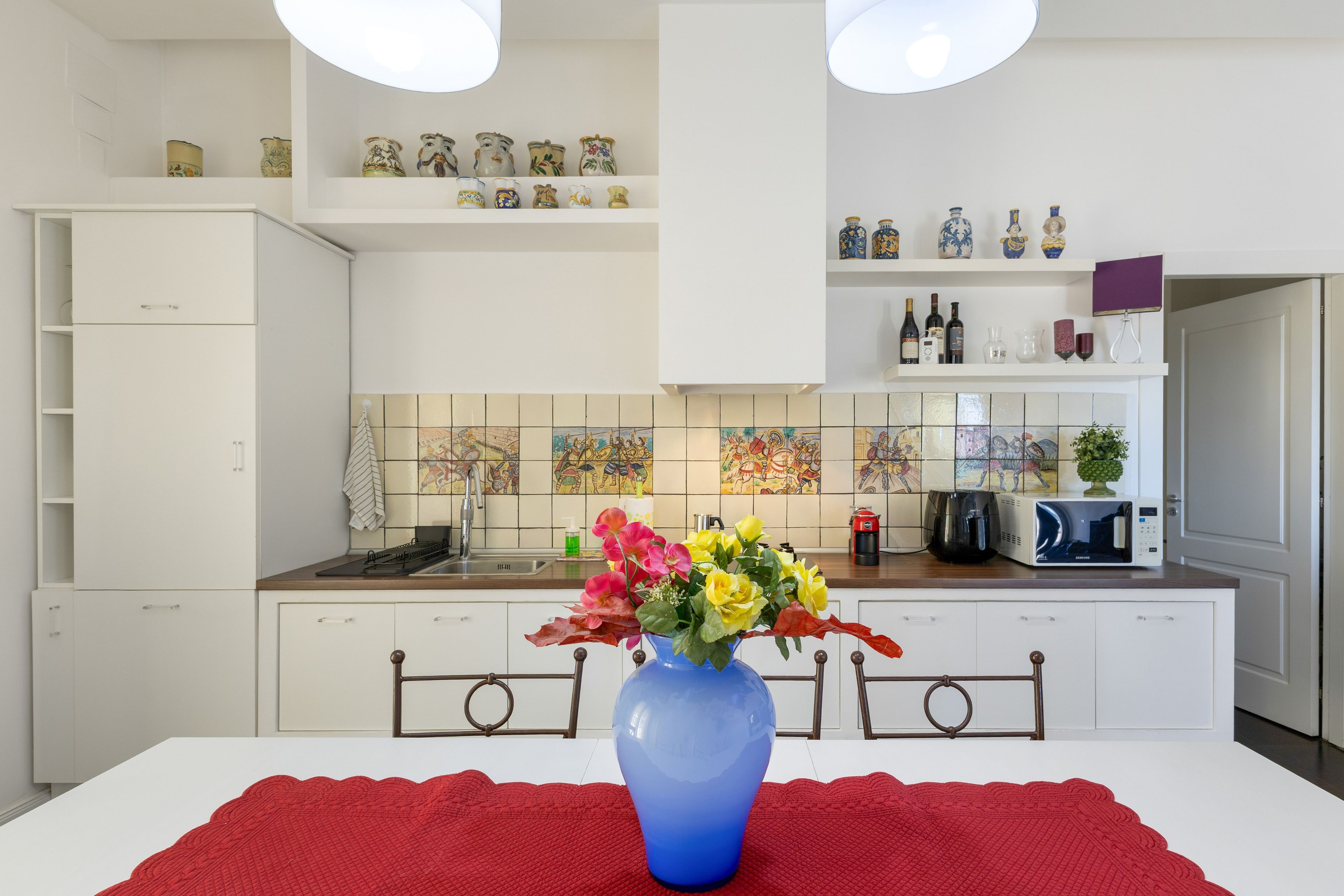 A modern kitchen with white cabinetry, a tiled backsplash, and a vase of flowers on the counter.