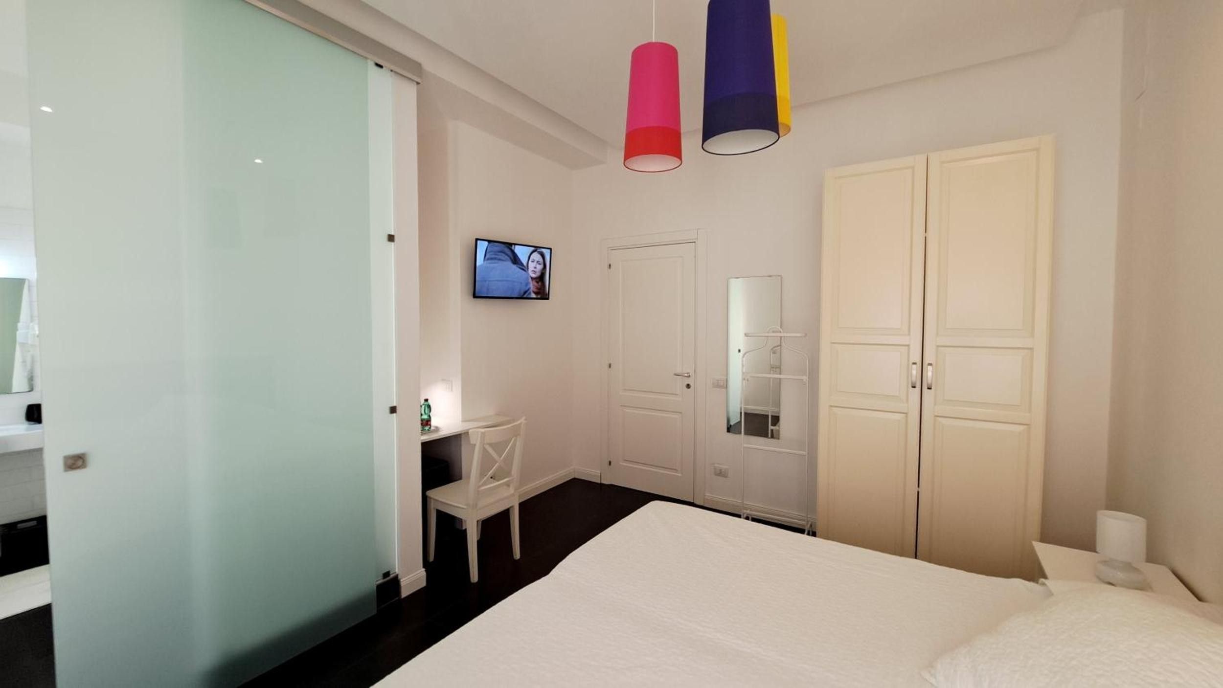 A bedroom with a bed, a desk, a chair, a television, and a wardrobe.