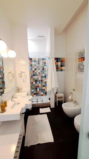 A modern bathroom with a white sink, a large mirror, a shower enclosure, and a bidet. - Casa Alba - Camera Elisa (Caltagirone)