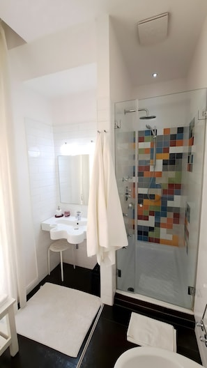 A modern bathroom with a glass-enclosed shower, a white sink, and a large mirror. - Casa Alba - Camera Elisa (Caltagirone)