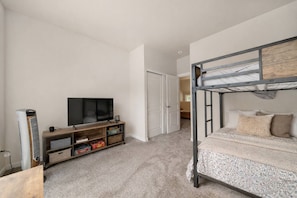 Een slaapkamer met een stapelbed, een televisie op een houten standaard en een deur naar een andere kamer.
