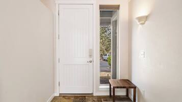 A hallway with a white door, a small wooden bench, and a view of a driveway with a parked vehicle.