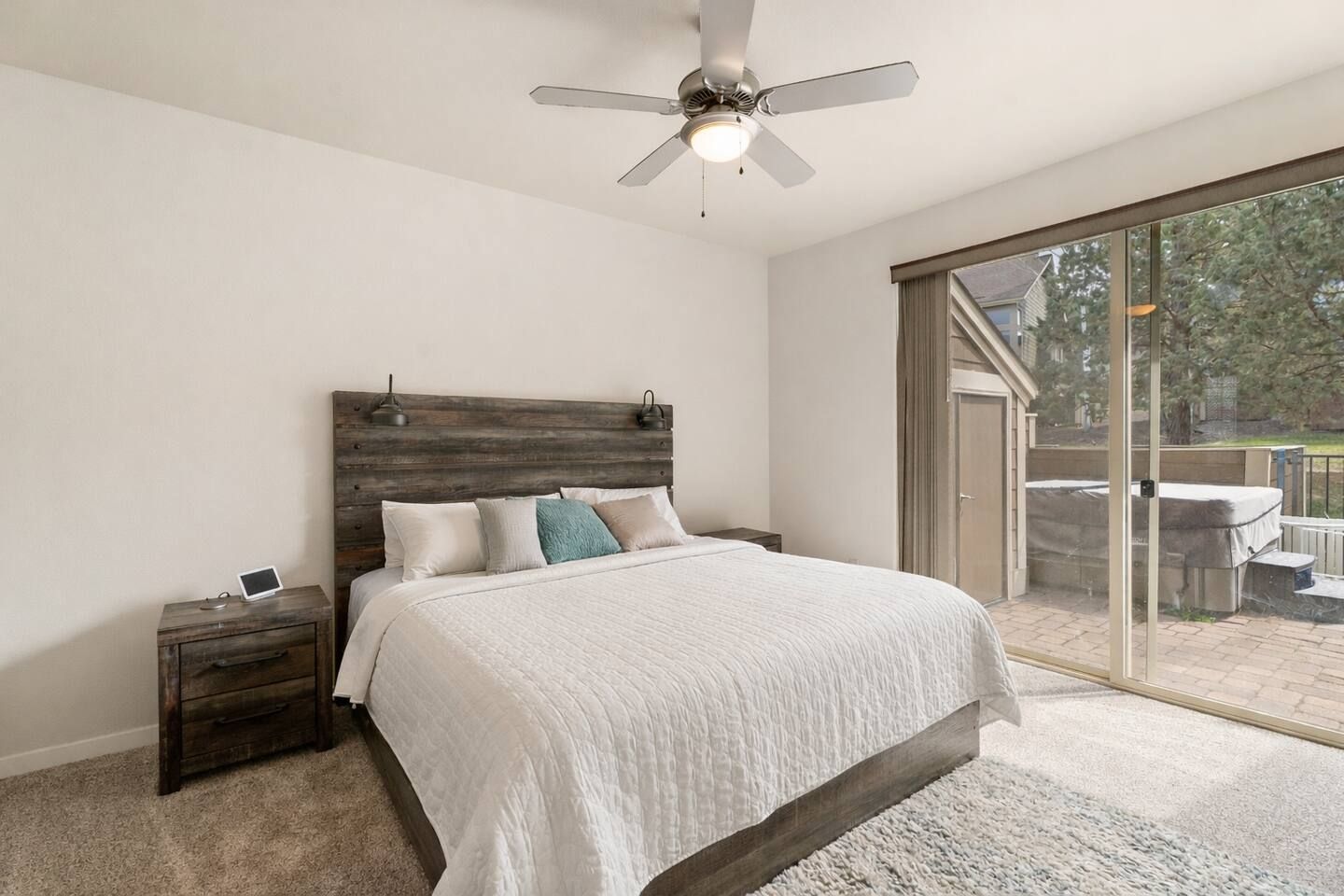 Un dormitorio con cama, mesita de noche, ventilador de techo y vistas al exterior.