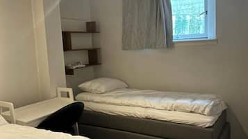 A small, single-bed room with a desk and chair, a window with a curtain, and built-in shelves.