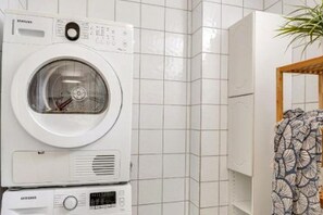 A front-loading washing machine in a bathroom with tiled walls and a wooden door. - 2-Bedroom Apartment with Private Entrance Near Tromsø City Centre (Tromsø)