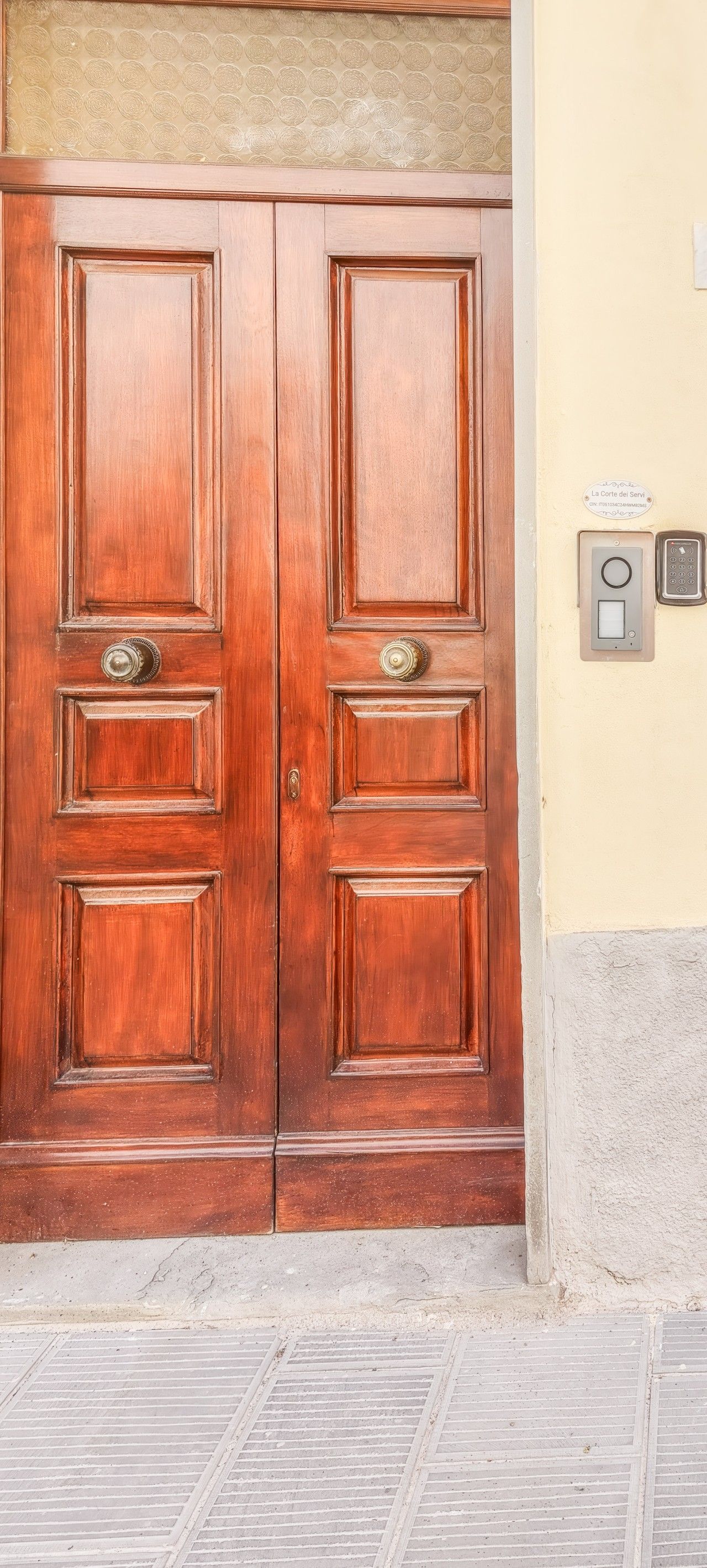 A wooden double door with a brass handle and a keypad lock on the wall beside it.
