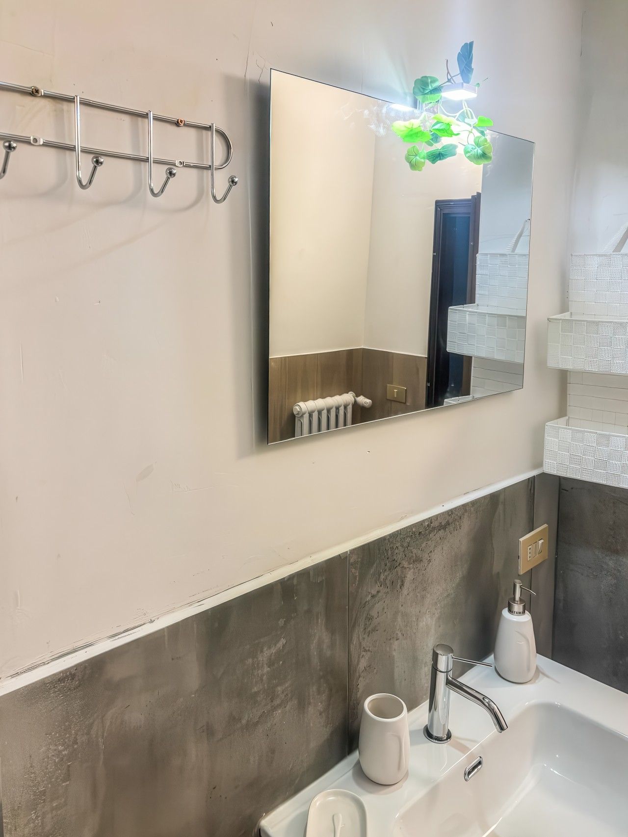 A modern bathroom with a large mirror, a towel rack, a radiator, a sink with a faucet, and a soap dispenser.
