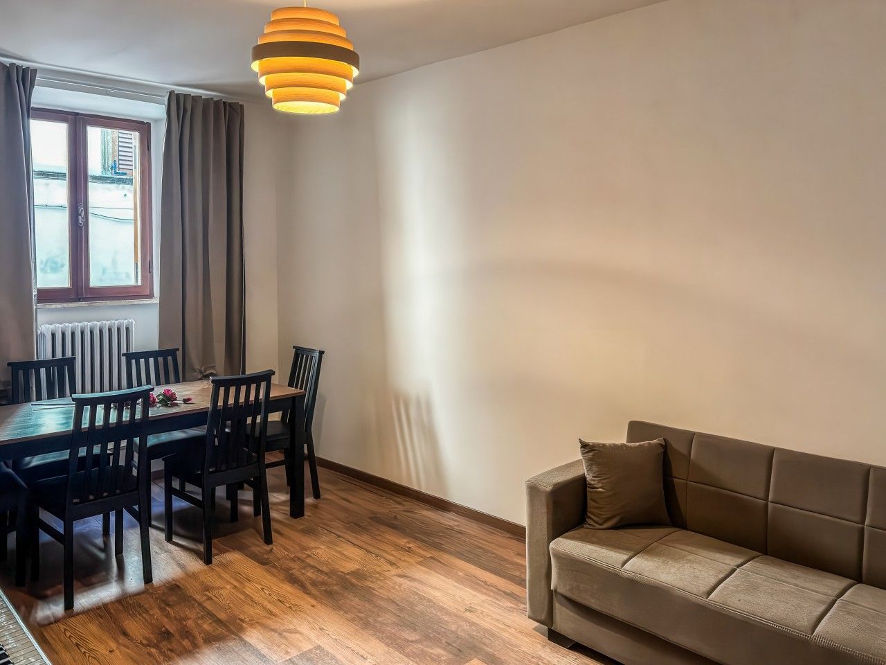 Ein Essbereich mit Holztisch und -stühlen, einer Couch und einer Pendelleuchte.
