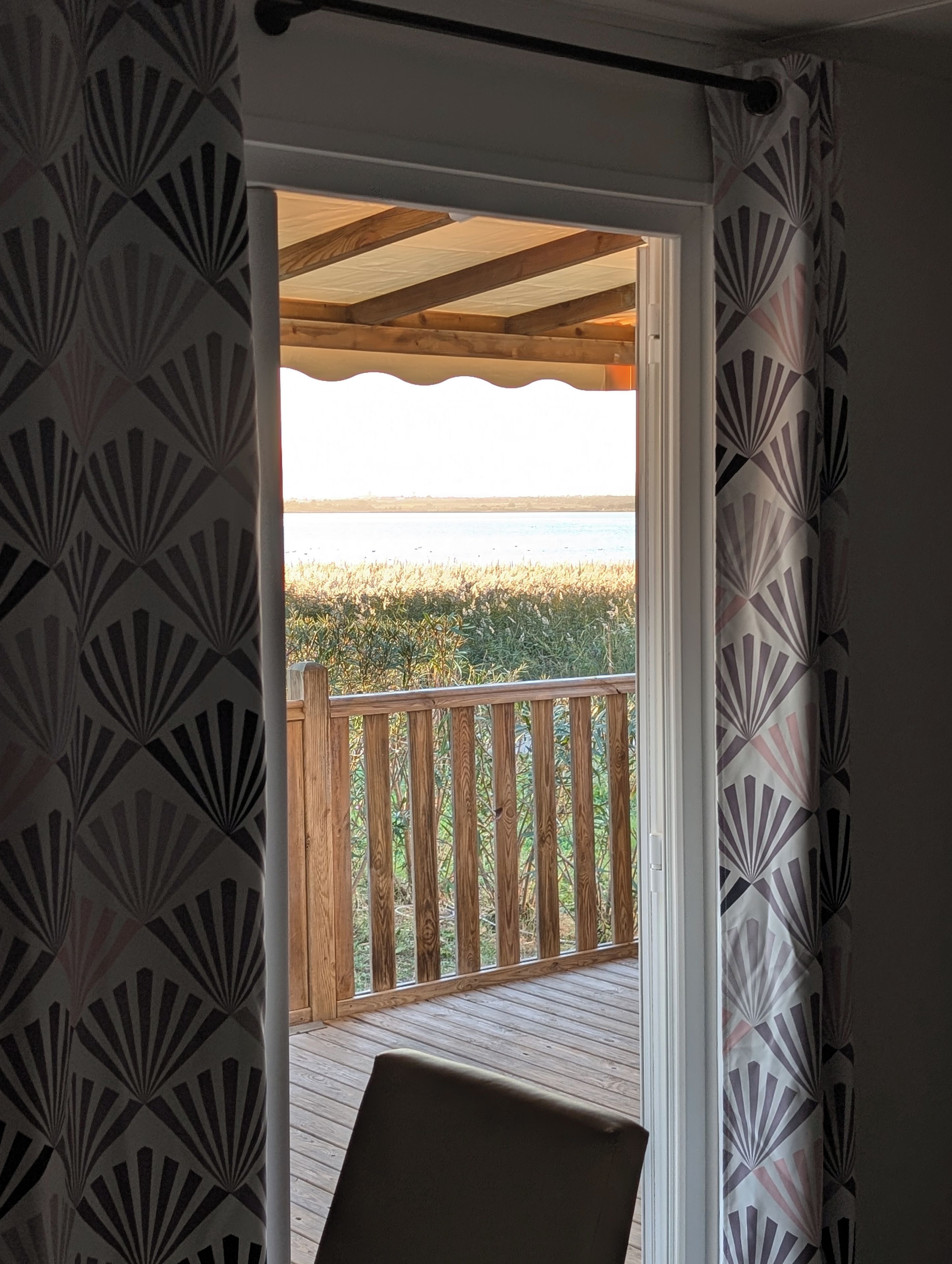 A room with a view of the beach, a wooden deck, and patterned curtains.