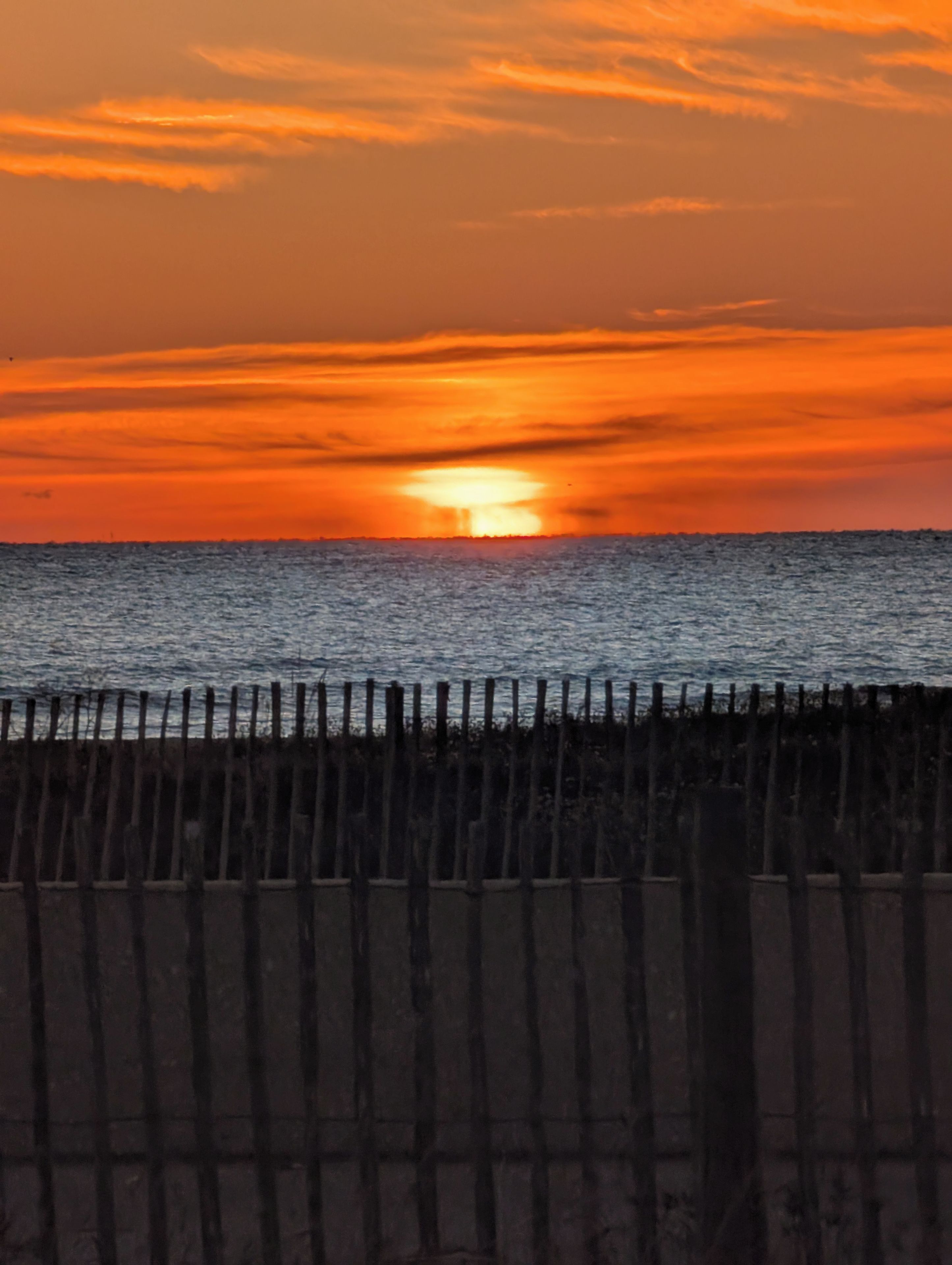 A sunset over a body of water with a wooden fence in the foreground.