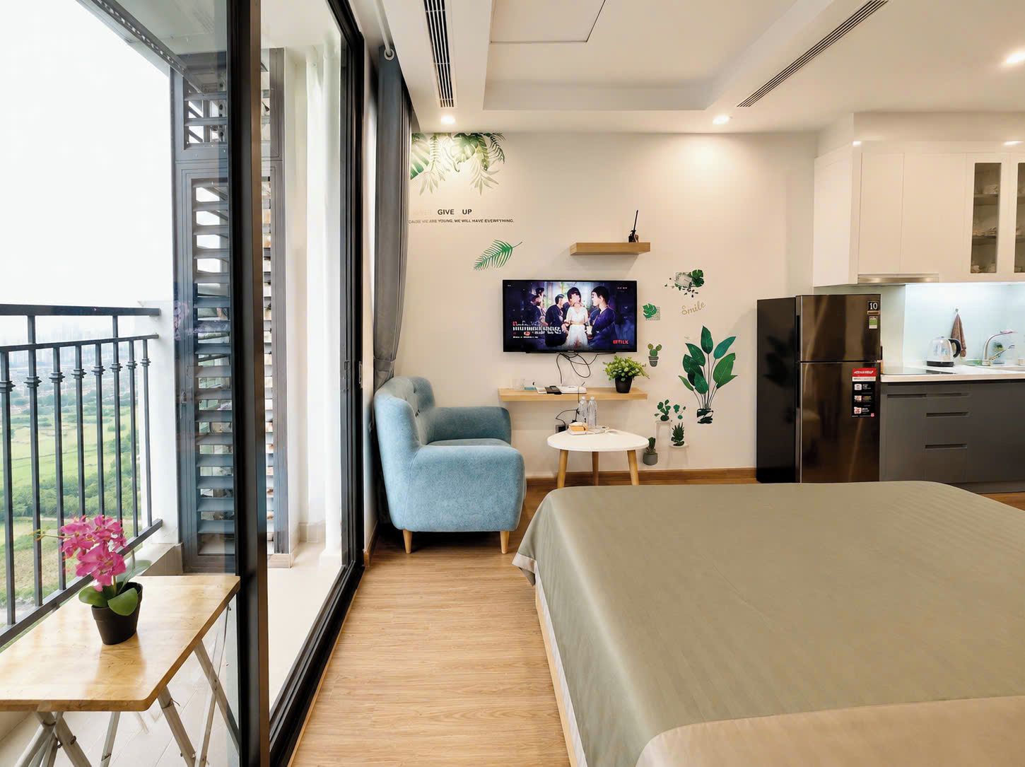 A modern bedroom with a bed, a seating area, a TV, and a kitchenette.