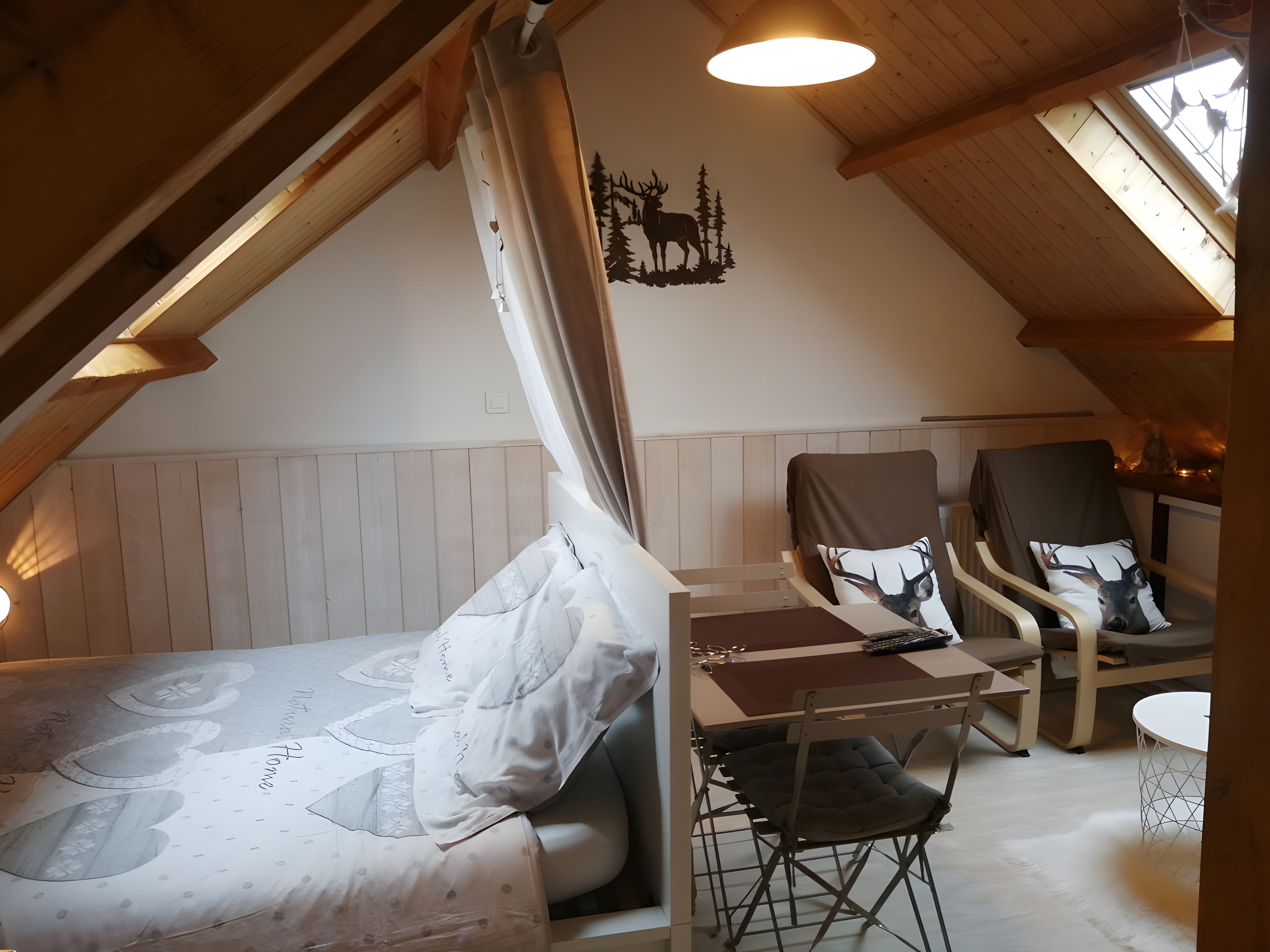 Een gezellig slaapkamer op zolder met een bed, twee stoelen, een klein tafeltje en een plafondlamp.