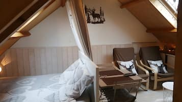 Een gezellig slaapkamer op zolder met een bed, twee stoelen, een klein tafeltje en een plafondlamp.