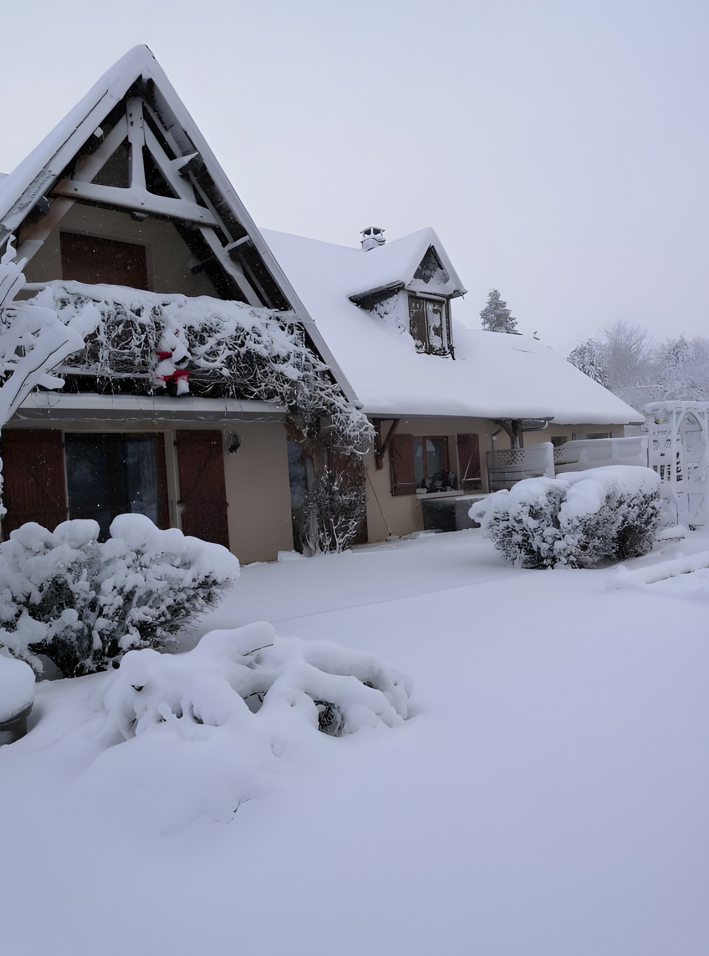 A house with a steeply pitched roof, a visible chimney, and a snow-covered front yard.