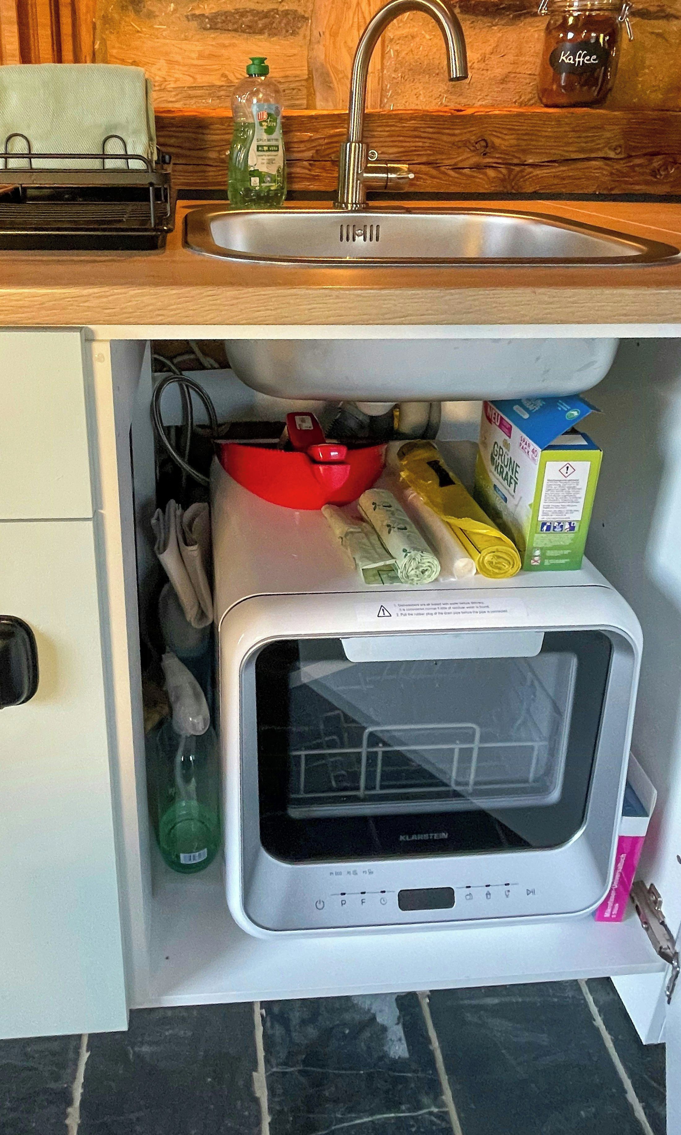 Eine Küche mit eingebauter Mikrowelle, einem Spülbecken und verschiedenen Küchenutensilien, die darunter aufbewahrt werden.