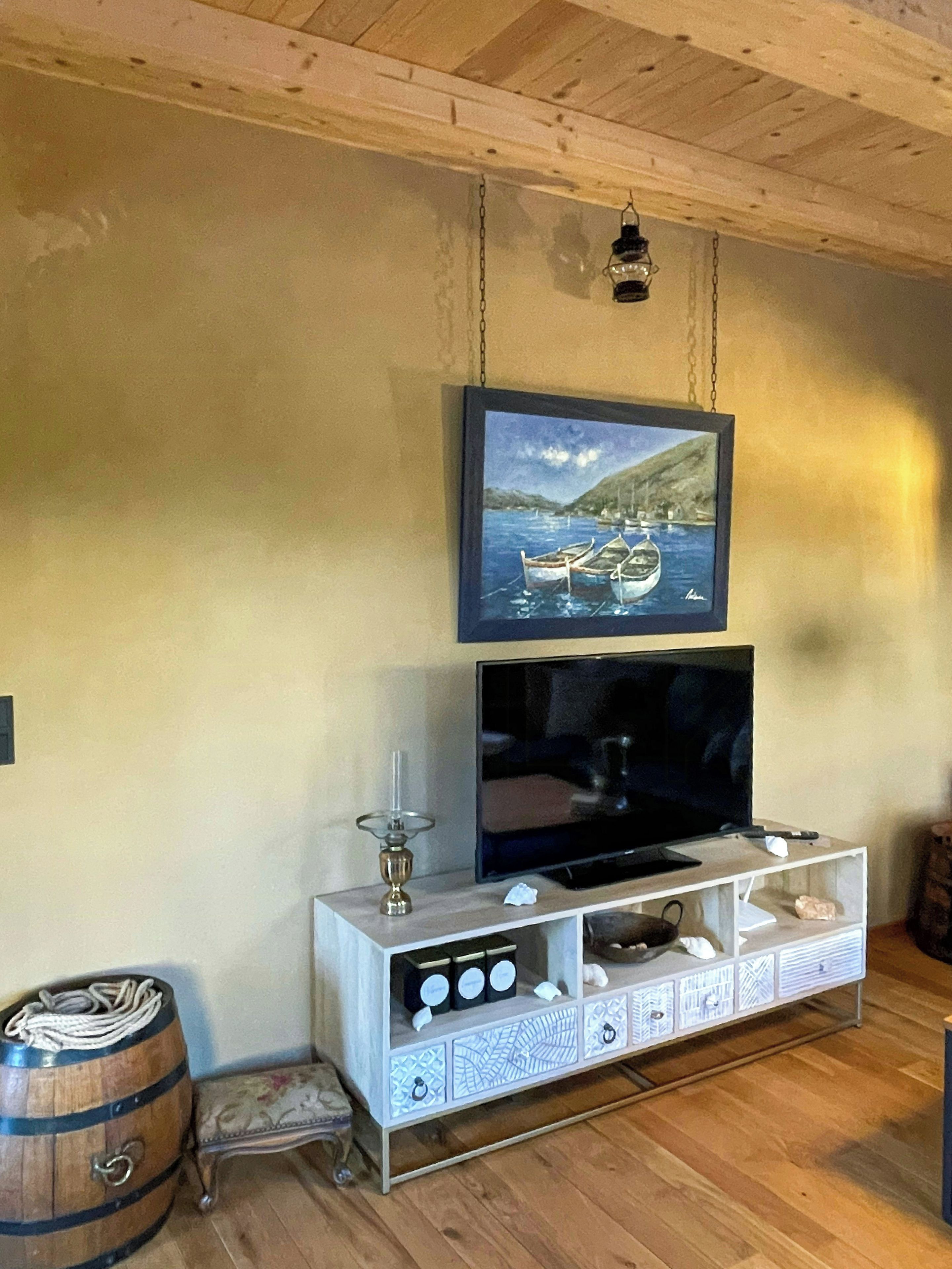 A wooden ceiling, a framed painting, a flat-screen TV, a cabinet with decorative patterns, and a wooden barrel.