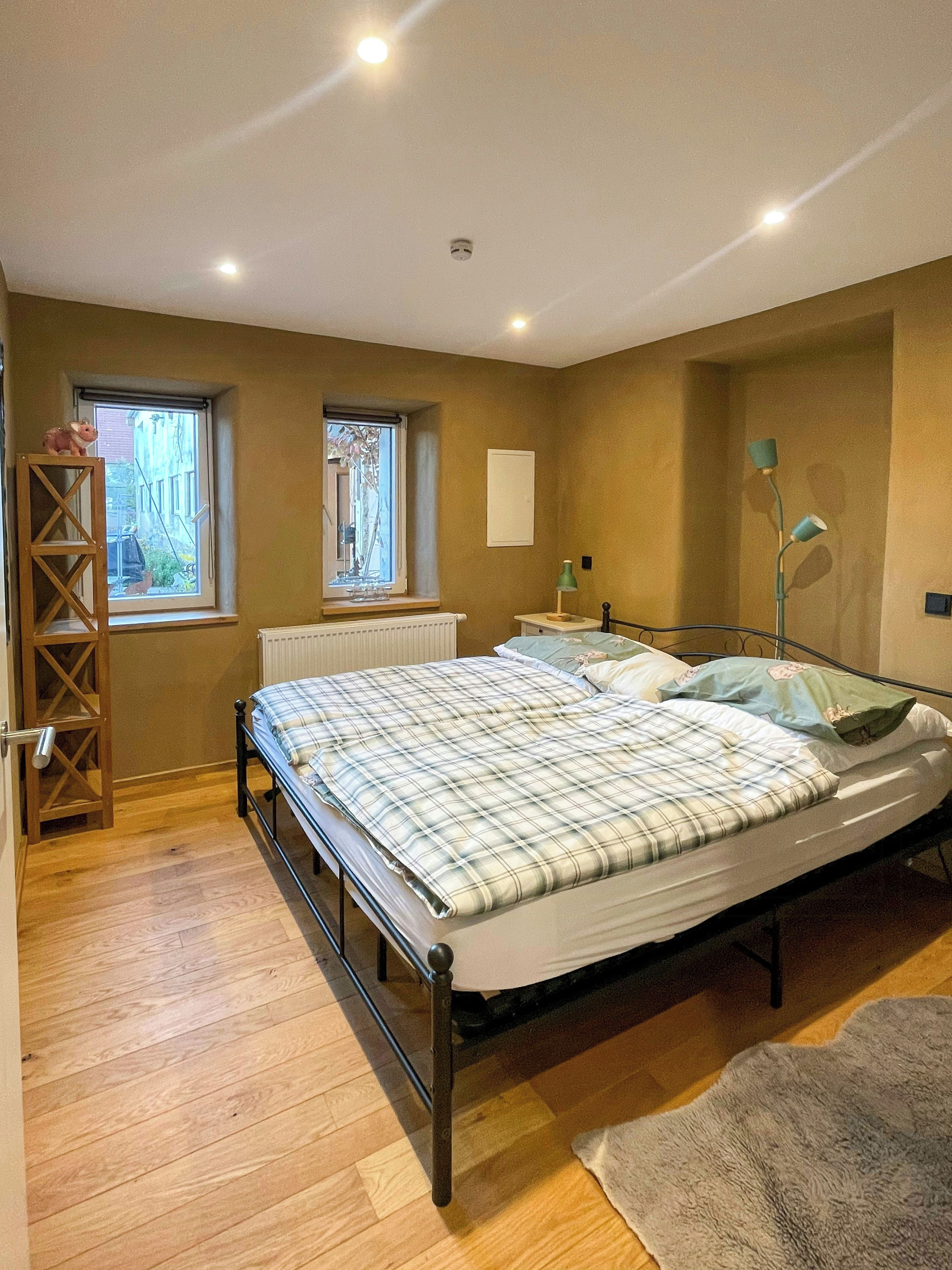 Ein Schlafzimmer mit einem Bett, einem Fenster, einem Heizkörper und einer Lampe.