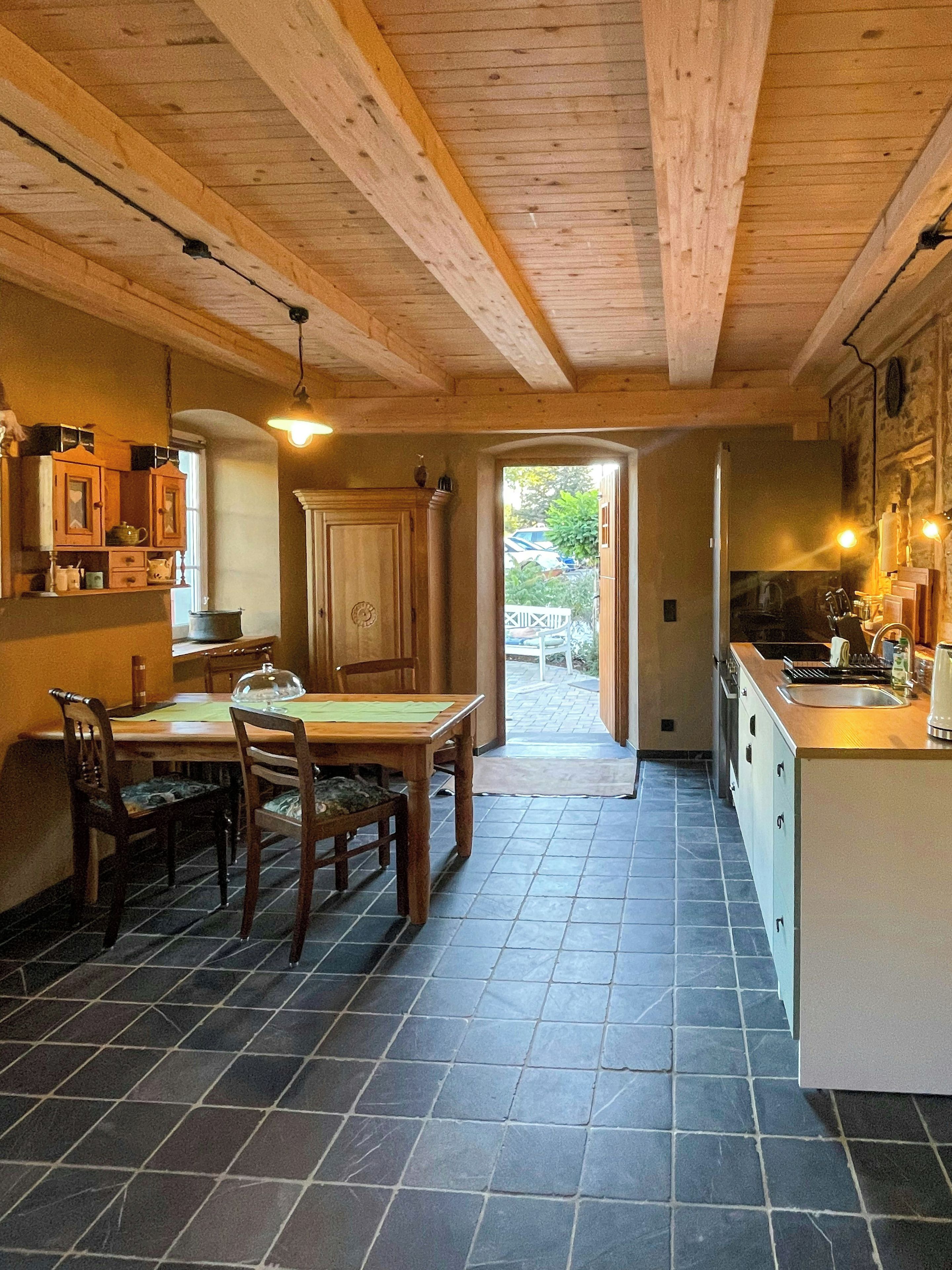 Ein Holzinterieur mit Esstisch und Stühlen, einer Küchenzeile und Blick durch einen offenen Durchgang.