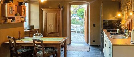 A wooden interior with a dining table and chairs, a kitchen area, and a view through an open doorway.