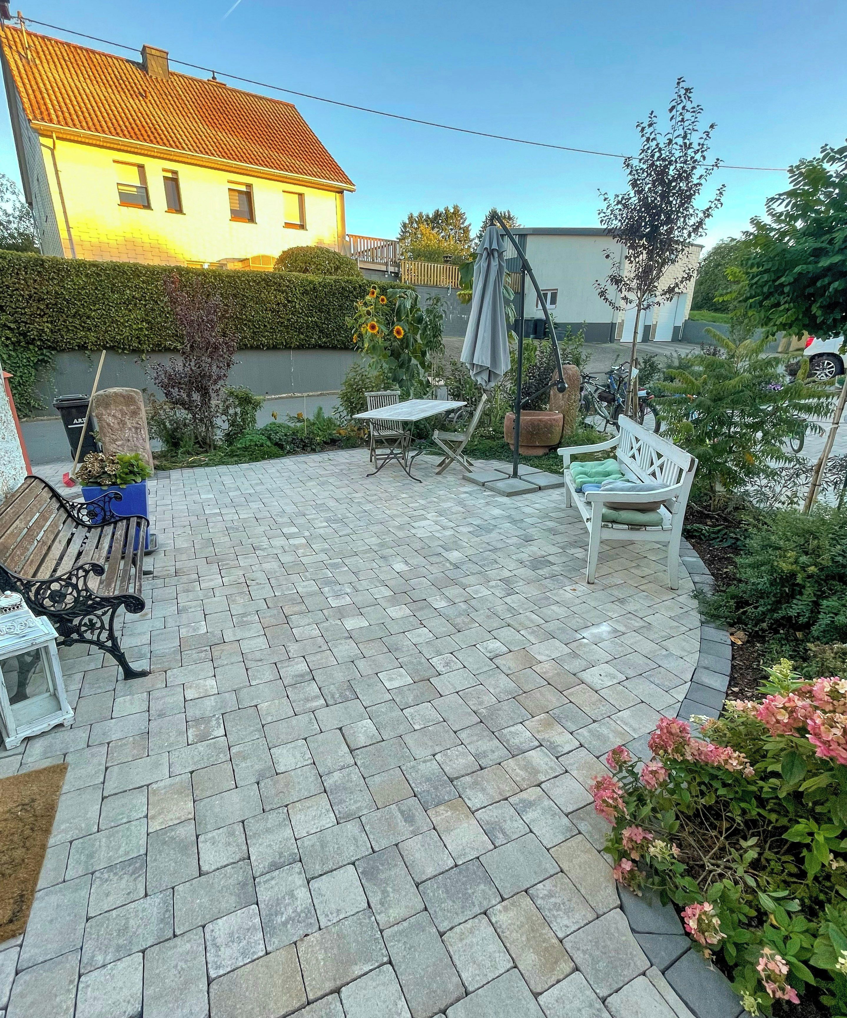 Een terras met stenen bestrating, een houten bank, een witte stoel en een tafel.