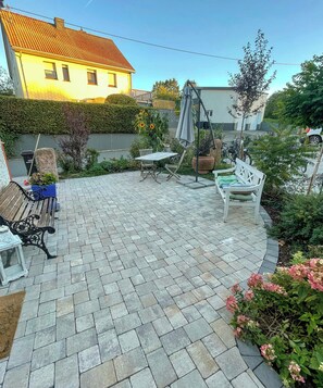 A patio area with stone paving, a wooden bench, a white chair, and a table. - Historic Apartment in the Eifel Village of Ormont (Ormont)