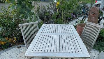 Una mesa de madera con patas metálicas, rodeada por un jardín con diversas plantas y flores.