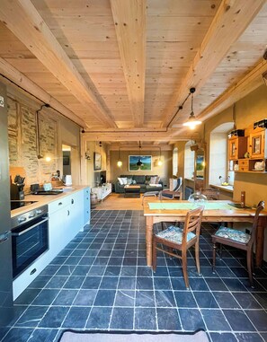 A cozy interior with a kitchen, dining area, and living space, featuring wooden beams, stone tiles, and modern appliances. - Historic Apartment in the Eifel Village of Ormont (Ormont)