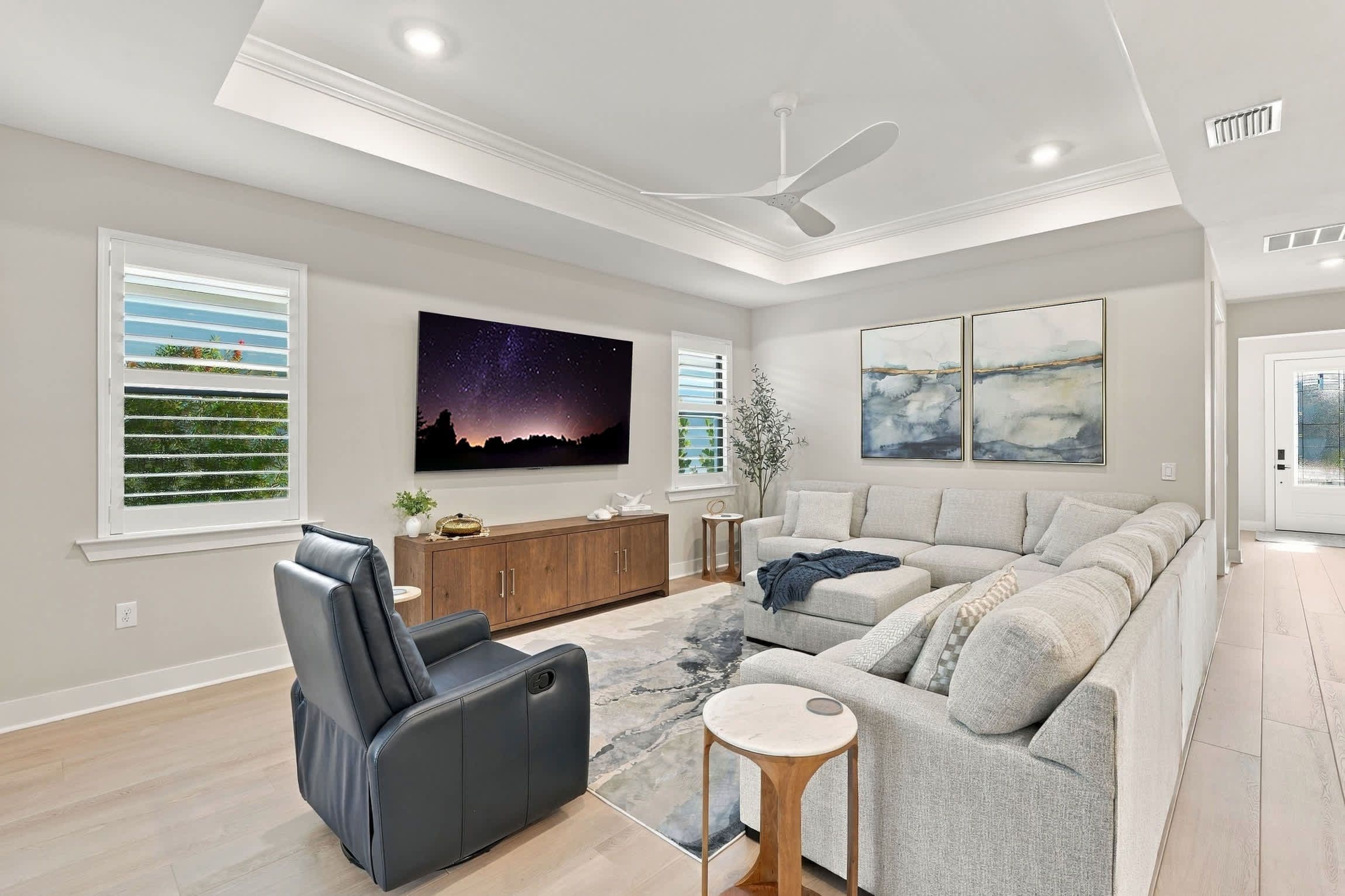 A modern living room with a sectional sofa, a recliner, a flat-screen TV, and artwork on the walls.
